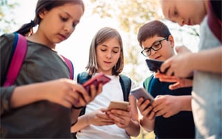 Four kids outside, each intent on a smartphone