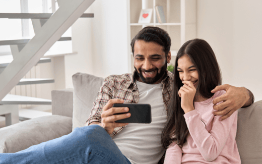 A parent and child smiling at a phone together