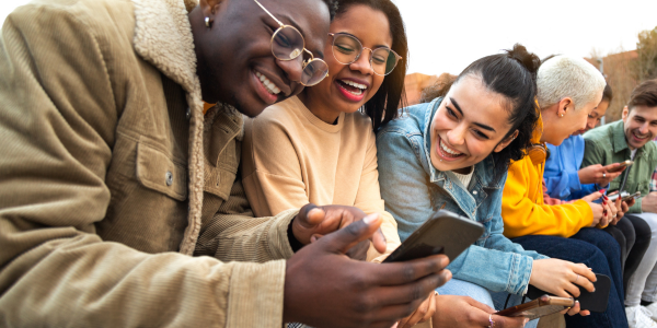 Two families laughing and using mobile devices together outside.