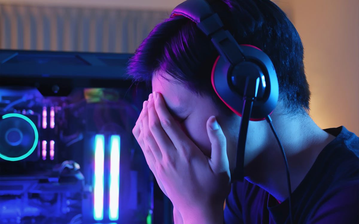 child with head in hands next to gaming computer