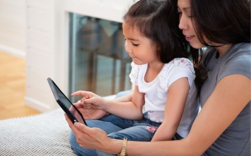 child in adult's lap using tablet together
