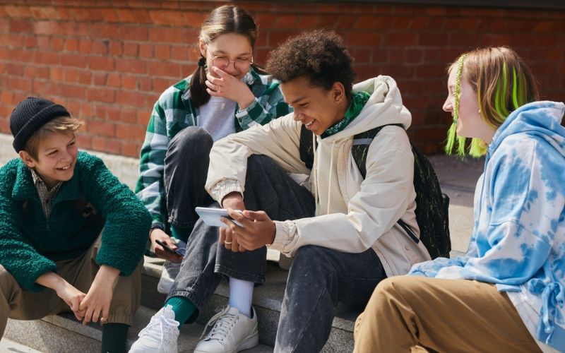 four young people laughing while viewing a phone outside school