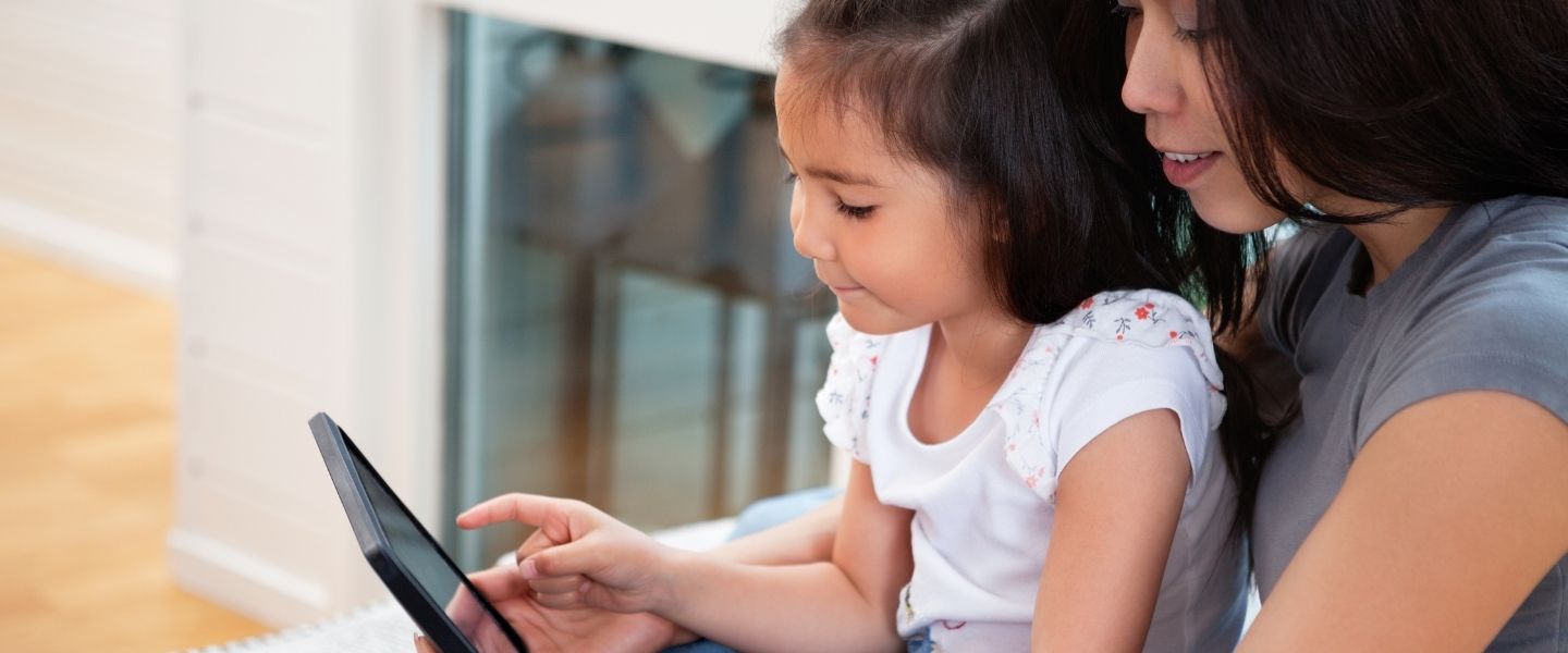 child in adult's lap using tablet together