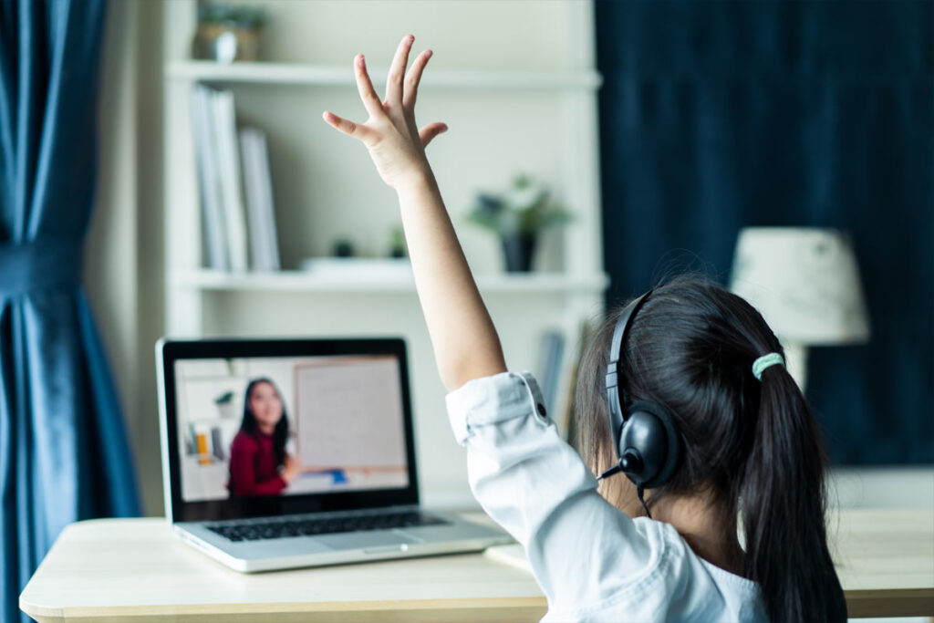 child raising hand in front of laptop elearning