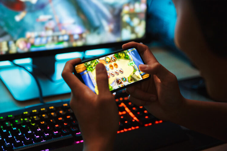 young person playing mobile game in front of gaming computer
