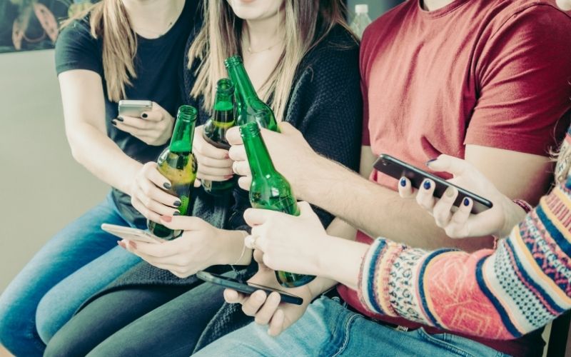 Young people with phones toasting with beer bottles