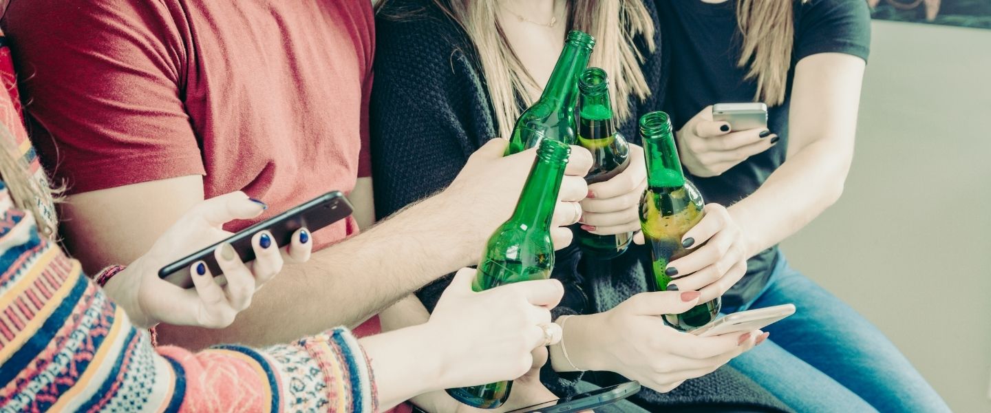 Young people with phones toasting with beer bottles