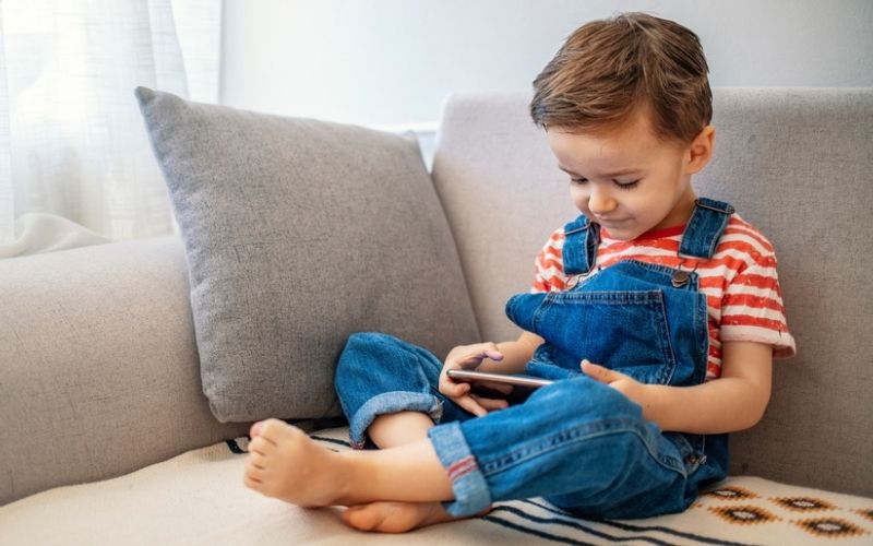 Very small child using phone on couch