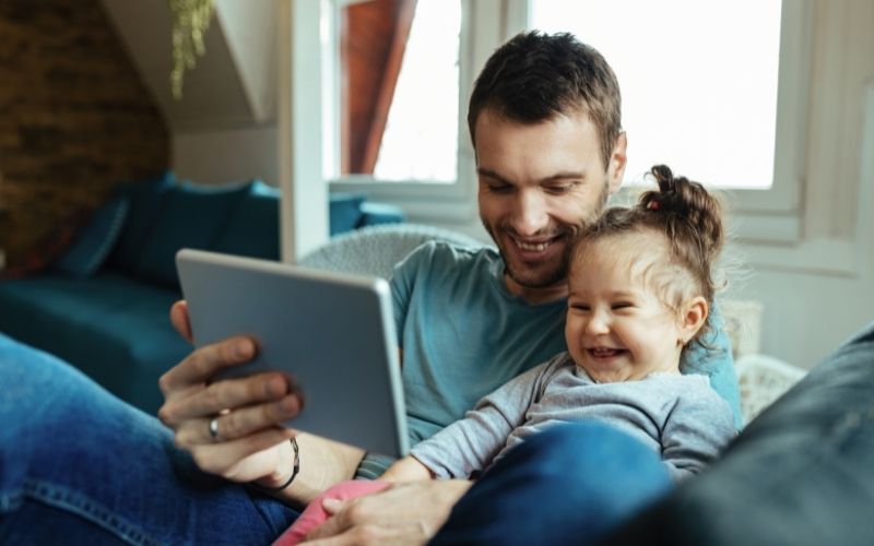 Toddler laughing, watching tablet with adult