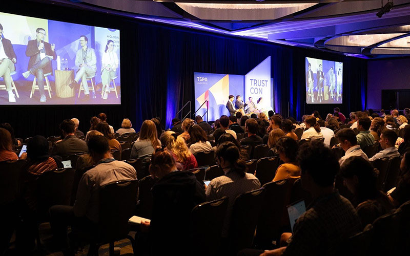 A packed house of conference attendees watches a panel discussion