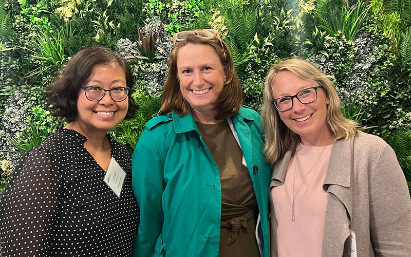 Cori and colleagues smiling in front of a lush garden background