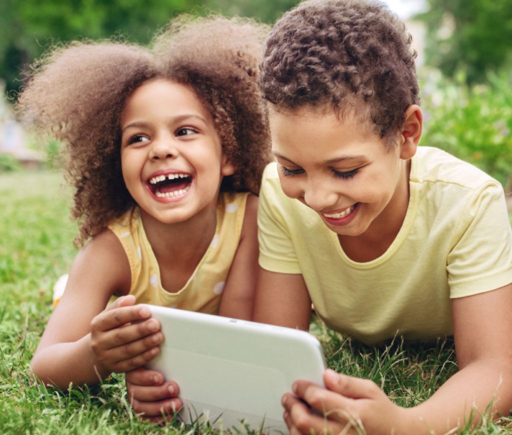 two youths happy with tablet on lawn