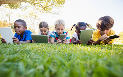 Five children with digital devices on a lawn