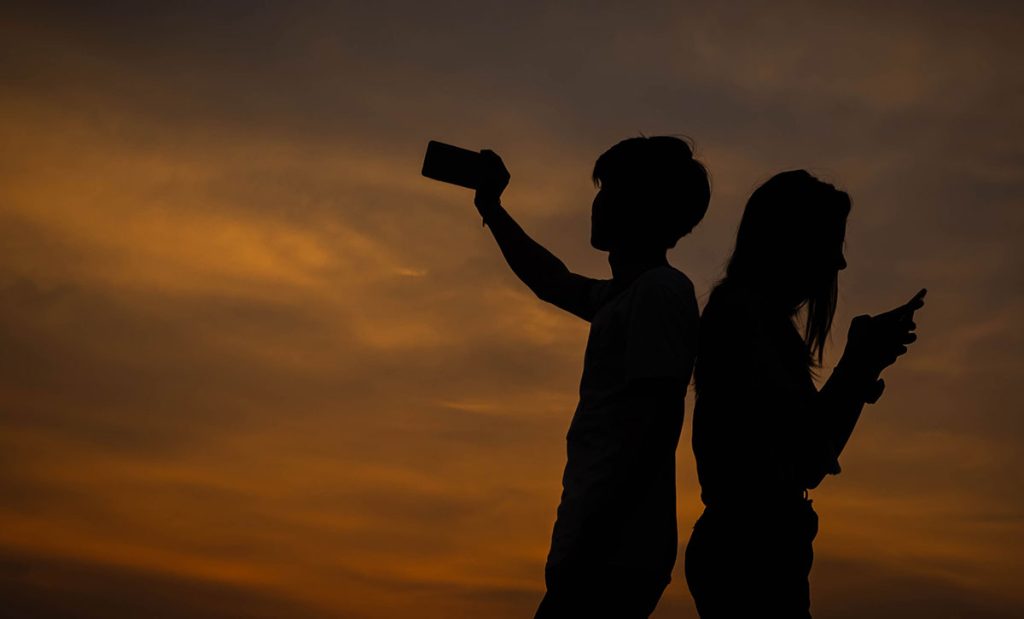 Pair of young people with mobile devices at dusk