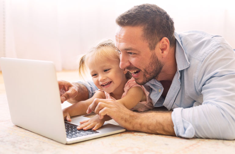 A parent with a child smiling at a laptop
