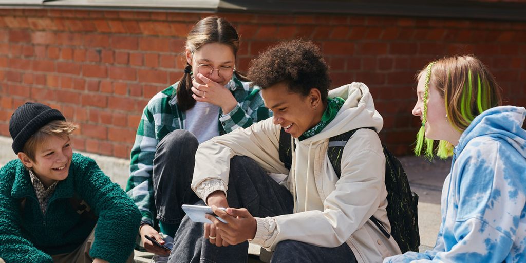 four young people laughing while viewing a phone outside school