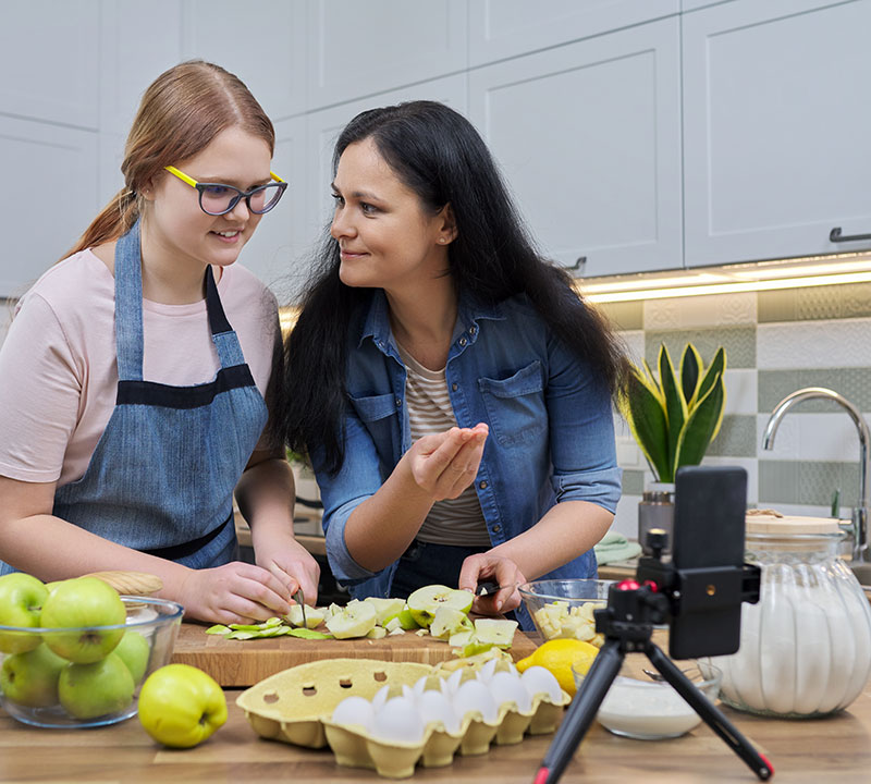 an adult and child cook together in front of a phone