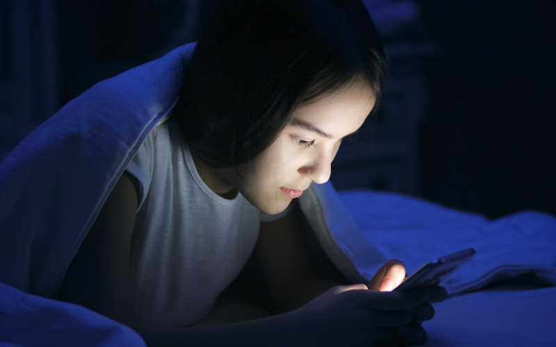 Young person using phone late at night in bed