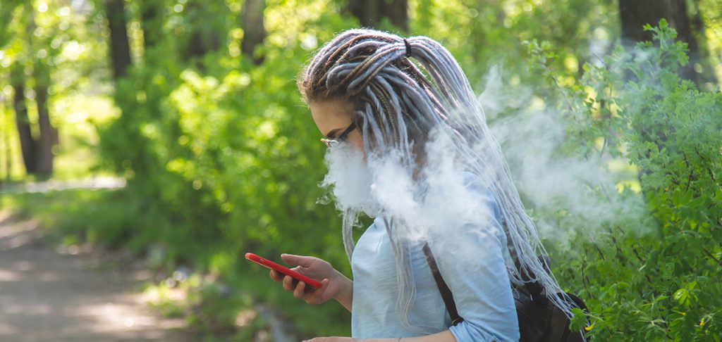 young person exhaling a cloud outside on their phone